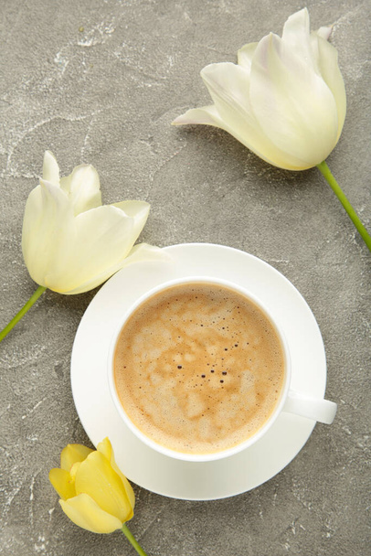 Cup of coffee with white tulips on grey background. Vertical photo. Top view - Fotografie, Obrázek