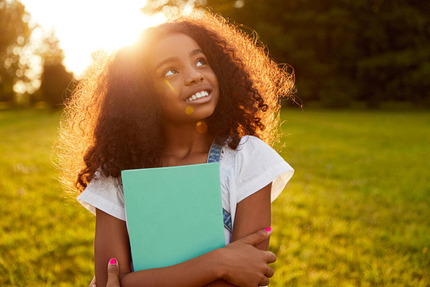 Black schoolgirl with notebook in park - Фото, зображення
