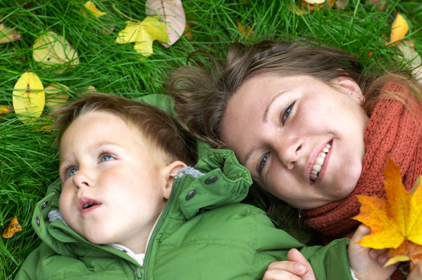 Smiling mother and son on the grass covered with fallen leaves - Fotoğraf, Görsel