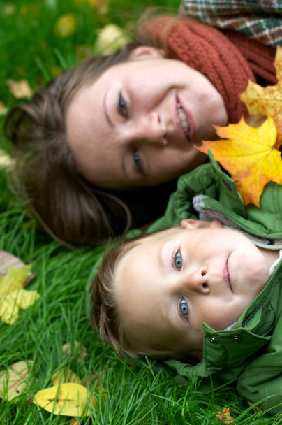 Smiling mother and son on the grass covered with fallen leaves - Foto, afbeelding