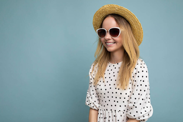 Fotografie záběr krásné pozitivní mladé blondýny žena na sobě letní ležérní oblečení a stylové sluneční brýle izolované přes barevné pozadí při pohledu do strany - Fotografie, Obrázek
