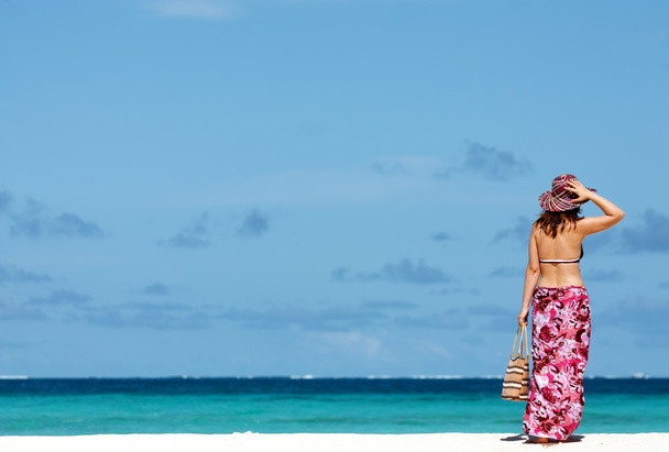 Young girl in sarong standing on white sandy beach looking to ocean - Foto, Imagen