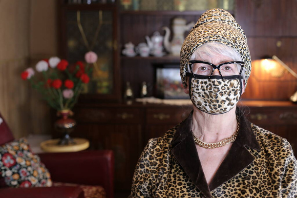 close-up portrait of mature woman in leopard pattern jacket with breath mask and hat at home - Φωτογραφία, εικόνα