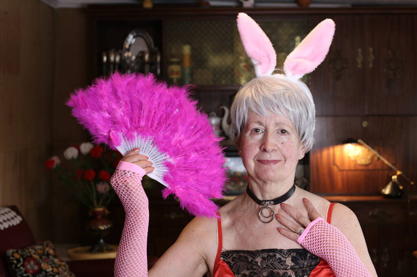 close-up portrait of mature woman in lingerie with bunny ears and handheld fan with feather at home - Fotoğraf, Görsel