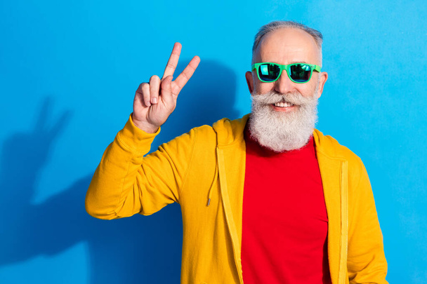 Photo of positive aged person toothy smile fingers show v-sign hello greetings isolated on blue color background - Fotoğraf, Görsel