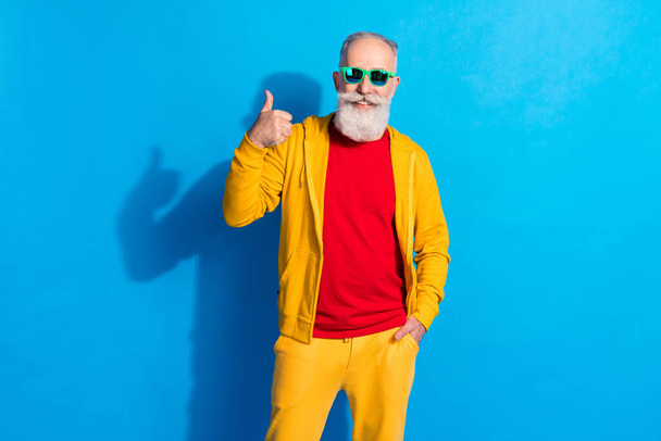 Photo of positive glad person toothy smile show thumb up put hand in pocket isolated on blue color background - Fotoğraf, Görsel