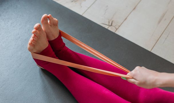 Resistance band exercise at home. Woman doing pilates workout using elastic strap pulling with arms for shoulder training on yoga mat indoors. Sport and healthy active lifestyle concept. - Foto, Imagen