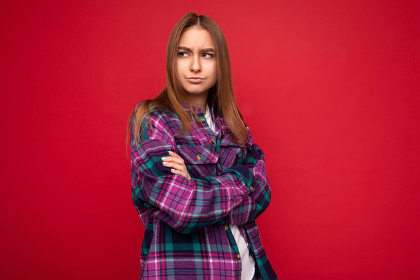 Photo shot of attractive sexy touchy upset young dark blonde woman isolated over red background wall wearing purple stylish shirt looking to the side keeping cross hands - Photo, Image