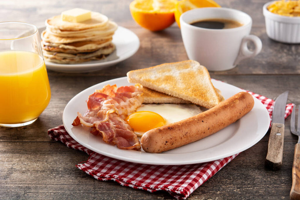 Traditional American breakfast with fried egg,toast,bacon and sausage on wooden table - Photo, Image