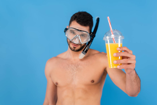 Orange juice in hand of blurred man in swimming goggles isolated on blue  - Photo, Image