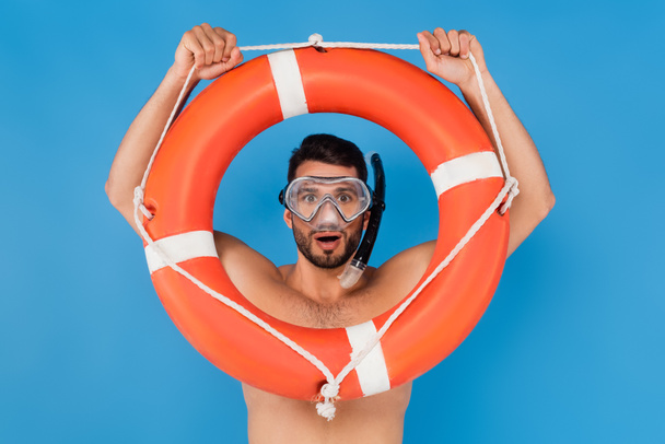 Excited man in swimming goggles holding life buoy isolated on blue  - Photo, Image