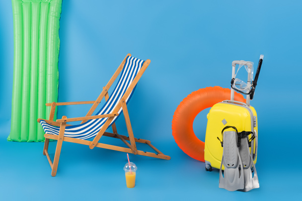 Deck chair near suitcase, swimming goggles and orange juice on blue background  - Foto, Imagem