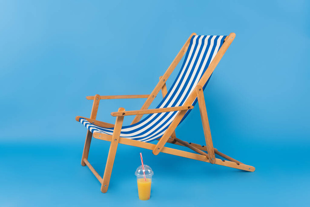 Jugo de naranja cerca de cubierta silla sobre fondo azul  - Foto, Imagen