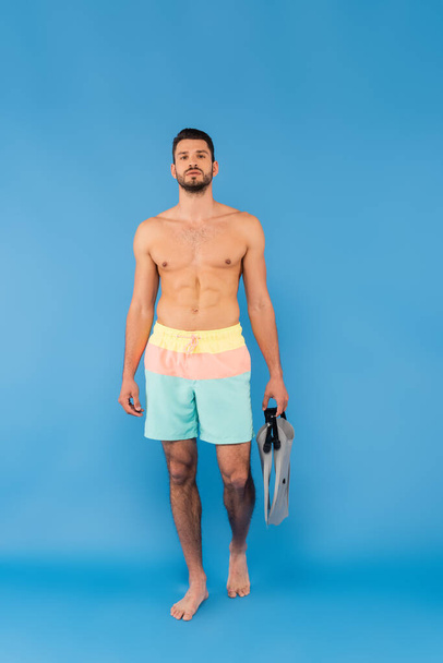 Muscular man holding swimming flippers on blue background  - Фото, зображення