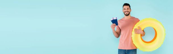 Θετικός άνθρωπος με διαβατήρια και φουσκωτά δαχτυλίδια απομονωμένος σε μπλε, banner  - Φωτογραφία, εικόνα