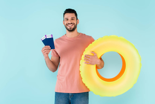 Happy man holding inflatable rings and passports isolated on blue  - Foto, Imagen