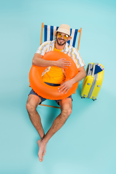 High angle view of happy man holding inflatable ring near suitcase and passports on blue background  - Photo, Image