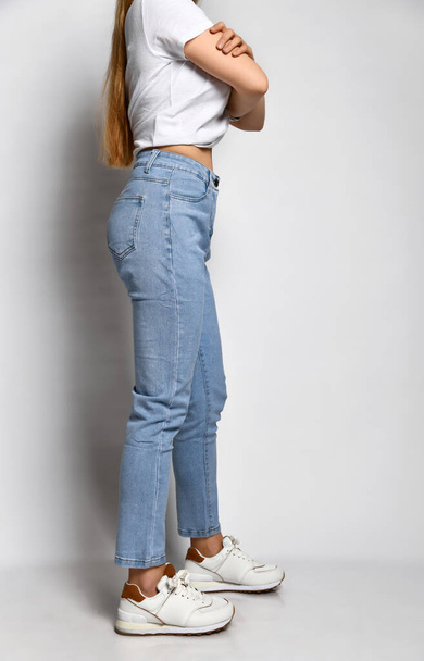 Unknown young skinny woman dressed in stylish blue jeans and white sneakers. - Foto, Imagem