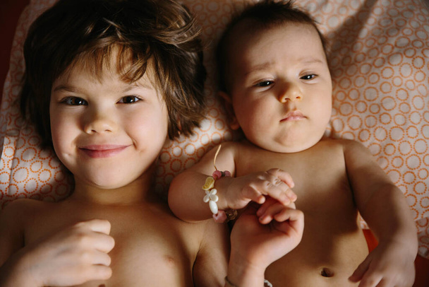 Girl and baby lying together on the pillow. Playing and smiling - Photo, Image