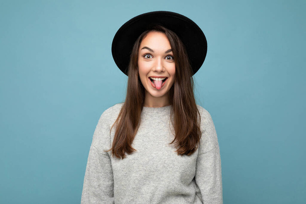 Retrato de linda atractiva bastante joven feliz mujer morena positiva usando suéter de rayas casuales aislado sobre fondo colorido con espacio de copia y mostrando la lengua - Foto, imagen