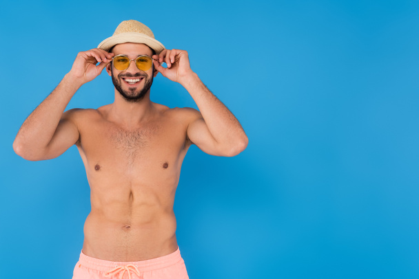 Cheerful shirtless man in sunglasses and straw hat on blue background  - Φωτογραφία, εικόνα