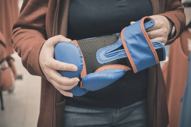 Femme en magasin choisit d'acheter des gants bleus pour une boxe. Mains en gros plan - Photo, image