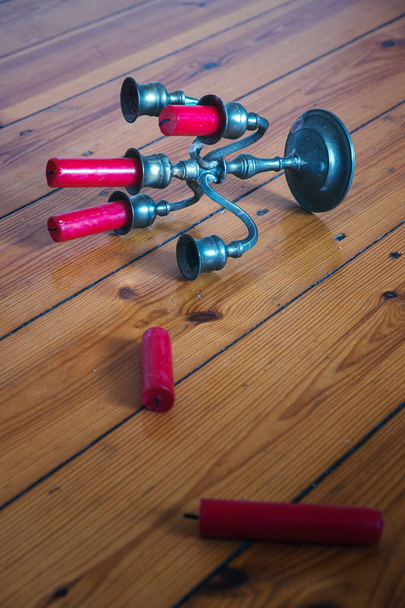 close-up of tin candleholder with red candles fallen on wooden floor  - Foto, imagen