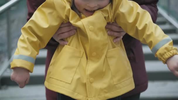 Moeder pakt een kind op in een geel jasje met een capuchon in haar armen - Video