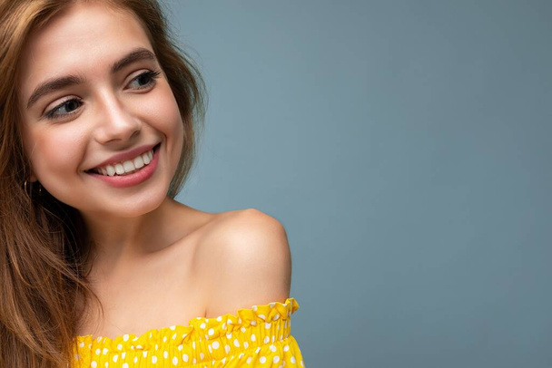 Closeup photo of young smiling cute beautiful dark blonde woman with sincere emotions isolated on background wall with copy space wearing stylish summer yellow dress. Positive concept - Фото, изображение