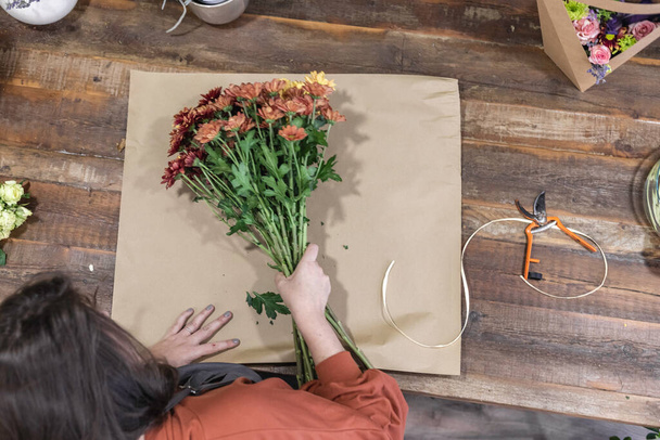 Zadní pohled na mladou ženu pracující jako květinářka a vytvářející krásné a barevné kytice na dřevěném stole, podnikatelka koncept. - Fotografie, Obrázek