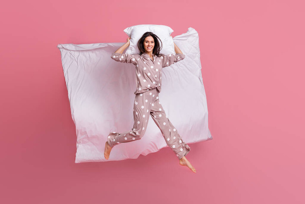 Photo of pretty adorable young woman dotted sleepwear jumping high lying pillow blanket isolated pink color background - Foto, immagini
