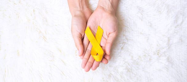 Рука держит желтую ленту на белом фоне для поддержки людей, живущих и больных. День профилактики самоубийств, концепция месяца информированности о раке саркомы и детства - Фото, изображение