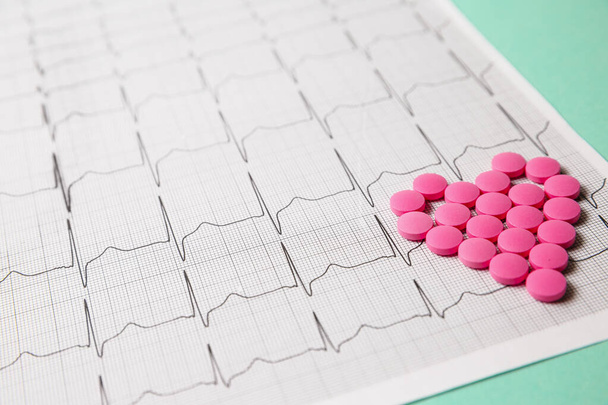 Una pila di pillole rosse a forma di cuore sul cardiogramma. Concetto medico. - Foto, immagini