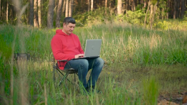Muž pracující na notebooku v letním lese - Záběry, video