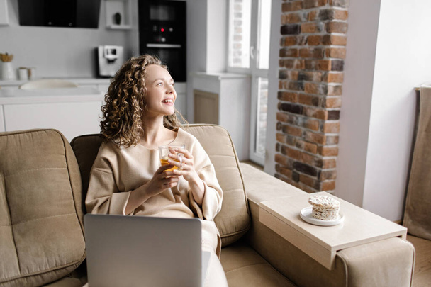 Femme heureuse assise sur le canapé en utilisant son ordinateur portable à la maison dans le salon. Je travaille de chez moi en quarantaine. Éloignement social Auto-isolement - Photo, image