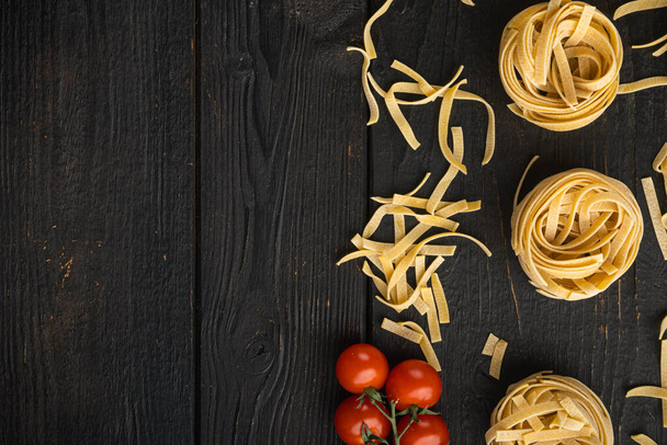 Gewalste tagliatelle vorm van Italiaanse pasta met ingrediënten set, op zwarte houten tafel achtergrond, bovenaanzicht plat lay, met kopieerruimte voor tekst - Foto, afbeelding