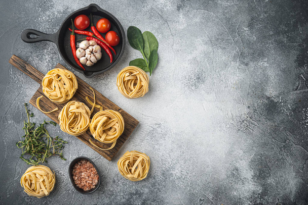 Rolled tagliatelle shape of italian pasta with ingredients set, on gray stone background, top view flat lay, with copy space for text - 写真・画像