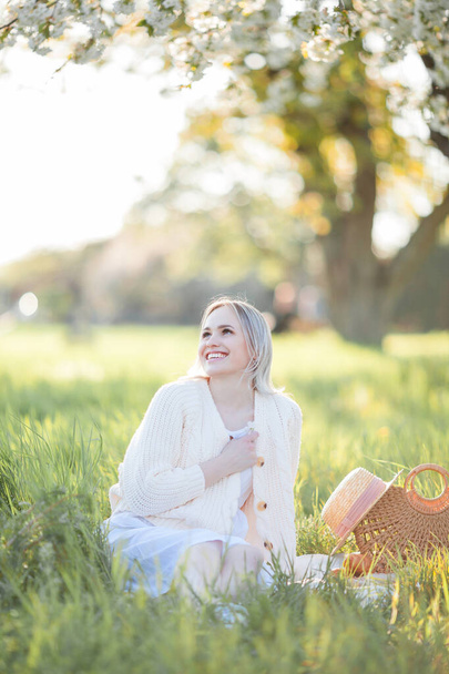 Όμορφη νεαρή γυναίκα ξεκουράζεται σε ένα πικνίκ σε έναν ανθισμένο κήπο. Λευκά λουλούδια. Άνοιξη. - Φωτογραφία, εικόνα