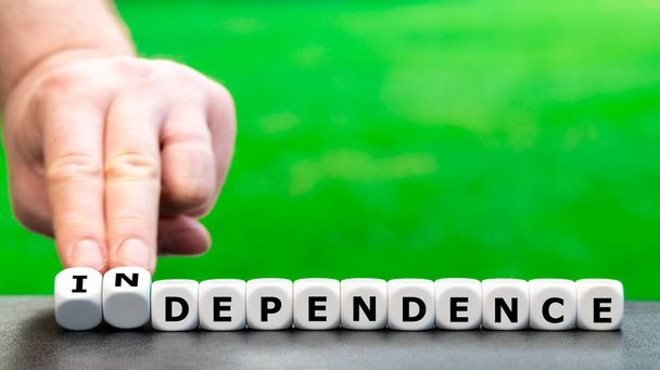 Hand turns dice and changes the word "dependence" to "independence". - Photo, Image