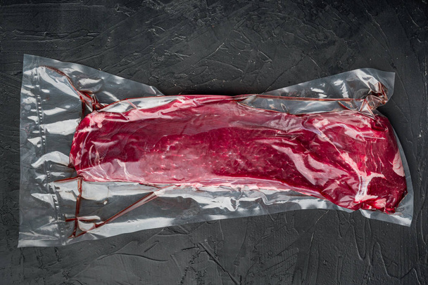 Fillet marhahús vákuum zsák sous vide készlet, fekete kő háttér, felső nézet lapos feküdt - Fotó, kép