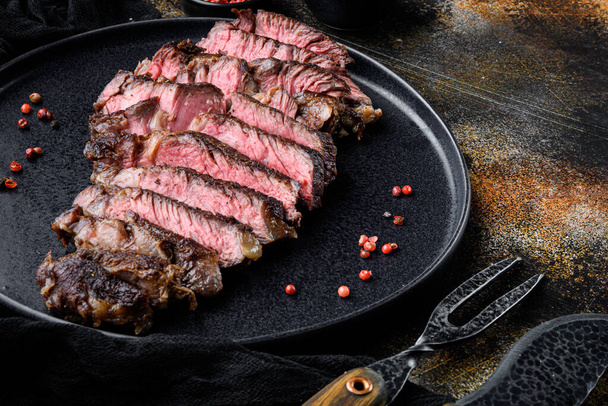 Grillezett vagy sült és szeletelt márványhús steak borda szem készlet, tányéron, húsvágó késsel és villával, régi sötét rusztikus háttérrel, szövegmásolási hellyel - Fotó, kép