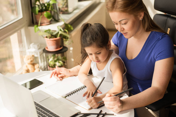 Mother explaining to her daughter how to do homework while sitting at the table - Photo, image