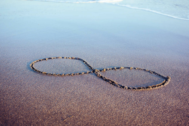 Eternity symbol on a wet glowing sand reflecting sky. Hand drawn 8 on a beach at seaside - Фото, зображення