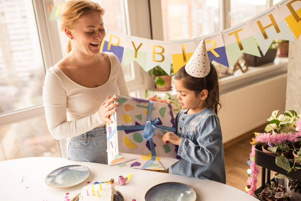 Woman giving a gift to her daughter wearing party cap while spending her birthday - Foto, immagini