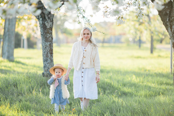 Una bella giovane madre con la sua figlioletta si riposa su un picnic nel giardino fiorito. Fiori bianchi. Primavera. - Foto, immagini
