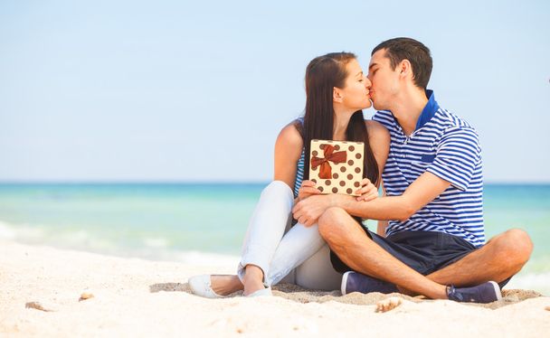 Jeune couple avec cadeau sur la plage en journée d'été
. - Photo, image