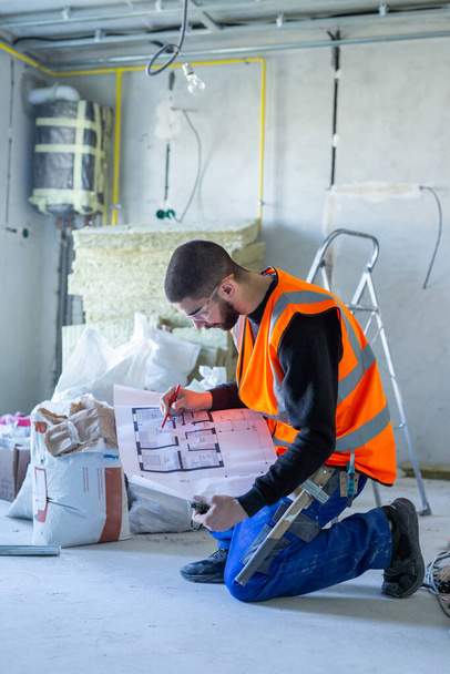 Hombre trabajador sosteniendo un plan de apartamento de papel interior antes de la sala de reparación  - Foto, Imagen