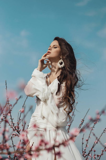 fashion outdoor photo of beautiful woman with dark hair in elegant dress posing in spring blooming garden - Fotó, kép