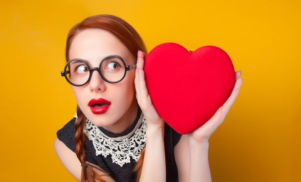 nerd κοκκινομάλλα κοπέλα με σχήμα καρδιάς σε κίτρινο backgorund. - Φωτογραφία, εικόνα