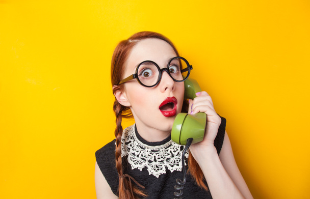 Redhead girl with green phone on yellow background. - Foto, Imagen